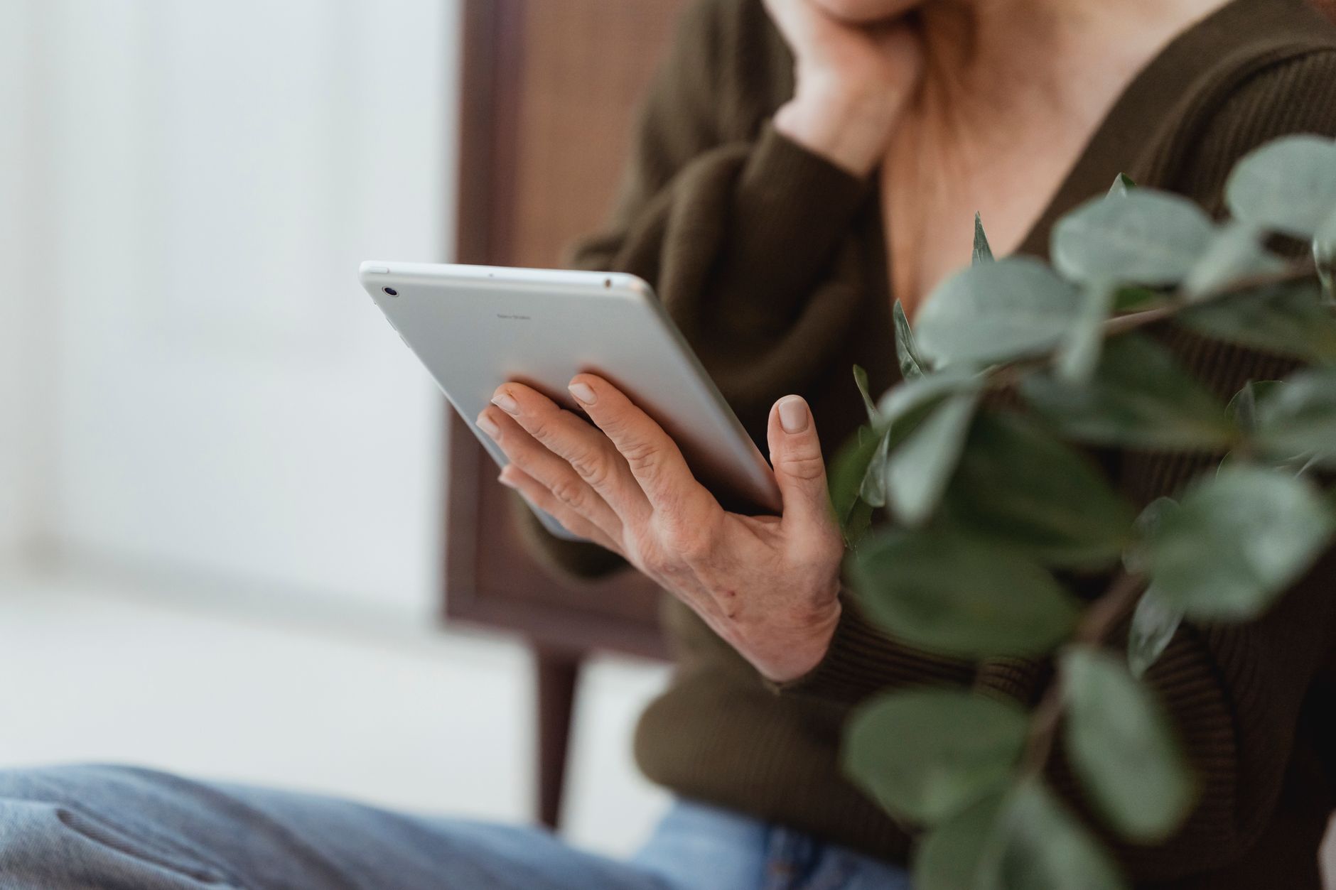 Close-up of a hand holding a silver tablet beside a leafy plant